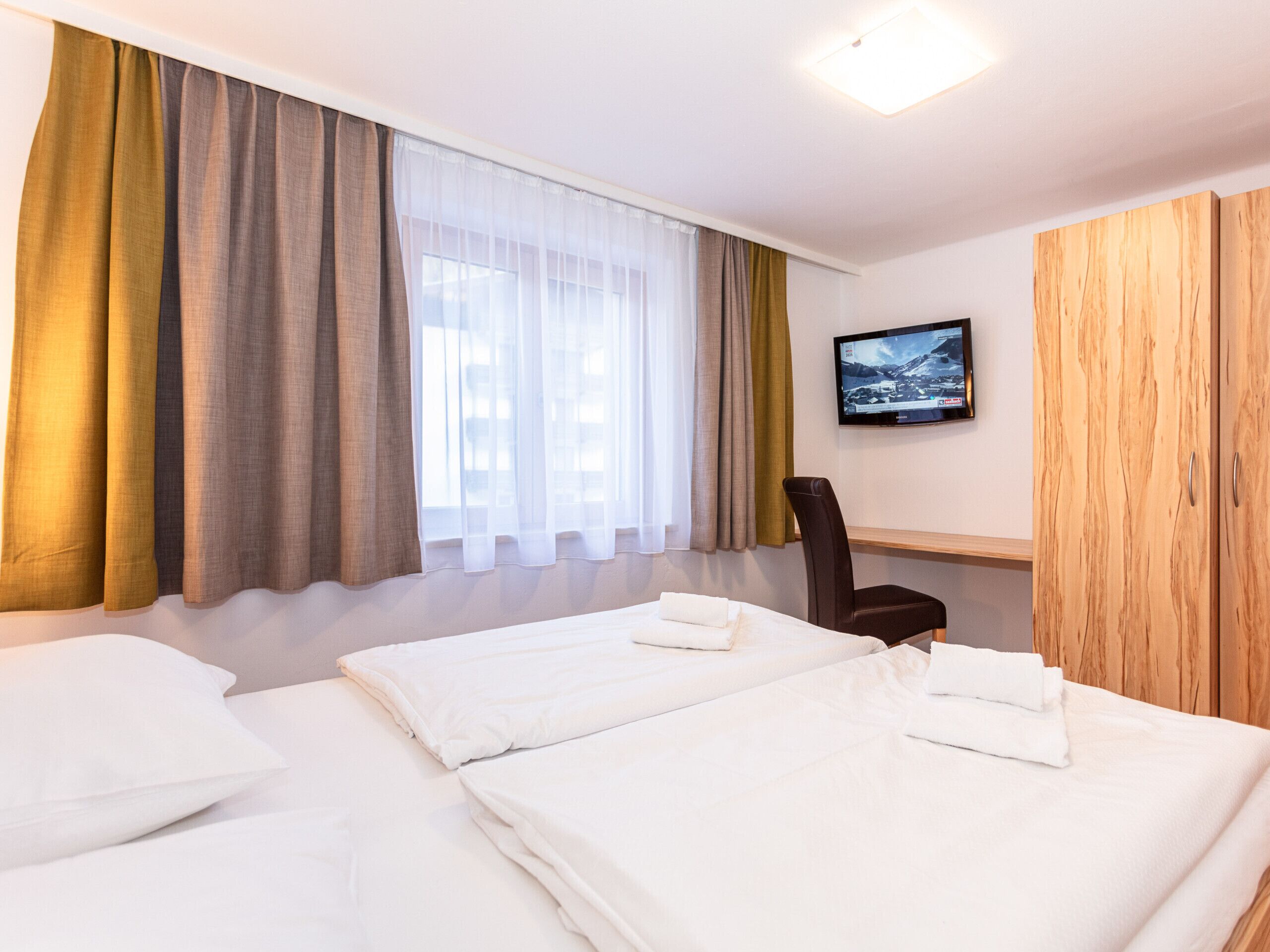 Une chambre d’hôtel avec deux lits, une télévision, une armoire en bois et une chaise.