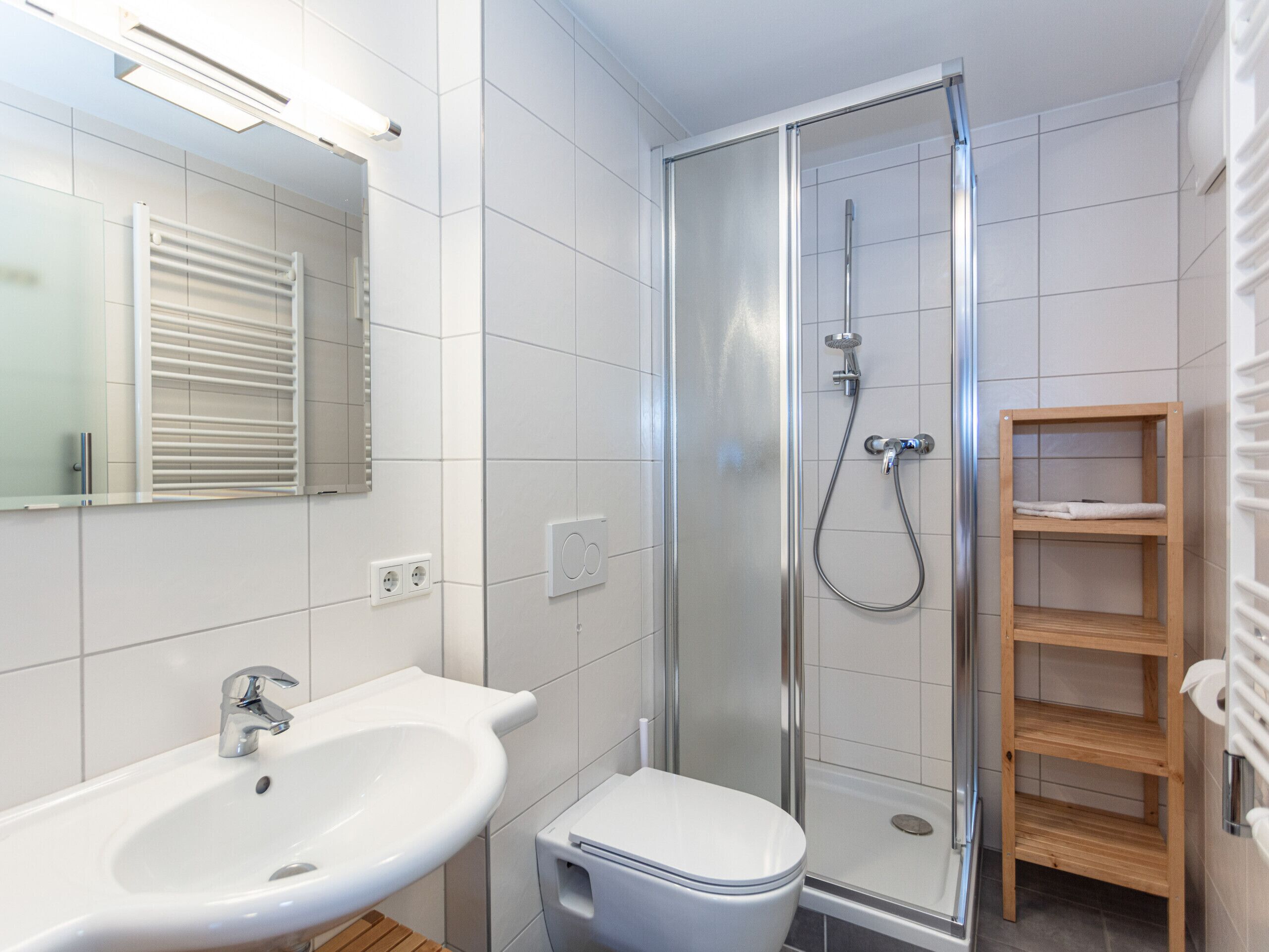 Un baño moderno con ducha, inodoro, lavabo y un estante de madera.