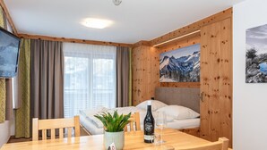 Una mesa de madera con sillas, una planta en maceta, una botella de vino y una copa.