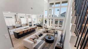 A spacious living area with a large L-shaped sectional sofa, a coffee table, and a dining area with a kitchen in the background. - Lux Lakefront with Game-room, Community Pool, Paddleboards, and more! (Willis)