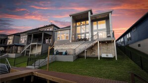 A modern multi-story residential building with a spacious deck area, multiple staircases, and a wooden deck leading to a pool. - Lux Lakefront with Game-room, Community Pool, Paddleboards, and more! (Willis)