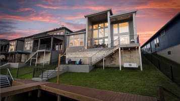 Un immeuble résidentiel moderne à plusieurs étages, doté d’une vaste terrasse, de plusieurs escaliers et d’une passerelle en bois menant à une piscine.