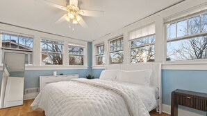 Un dormitorio con cama, ventilador de techo y ventanas amplias.