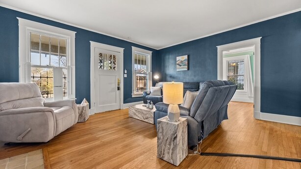 Una sala de estar con una pared azul, piso de madera, un sofá gris, un sofá azul, una mesa de centro de mármol y una lámpara.