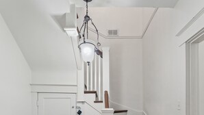 Una escalera de madera con paredes blancas que conduce a un rellano con una puerta y una lámpara arriba.