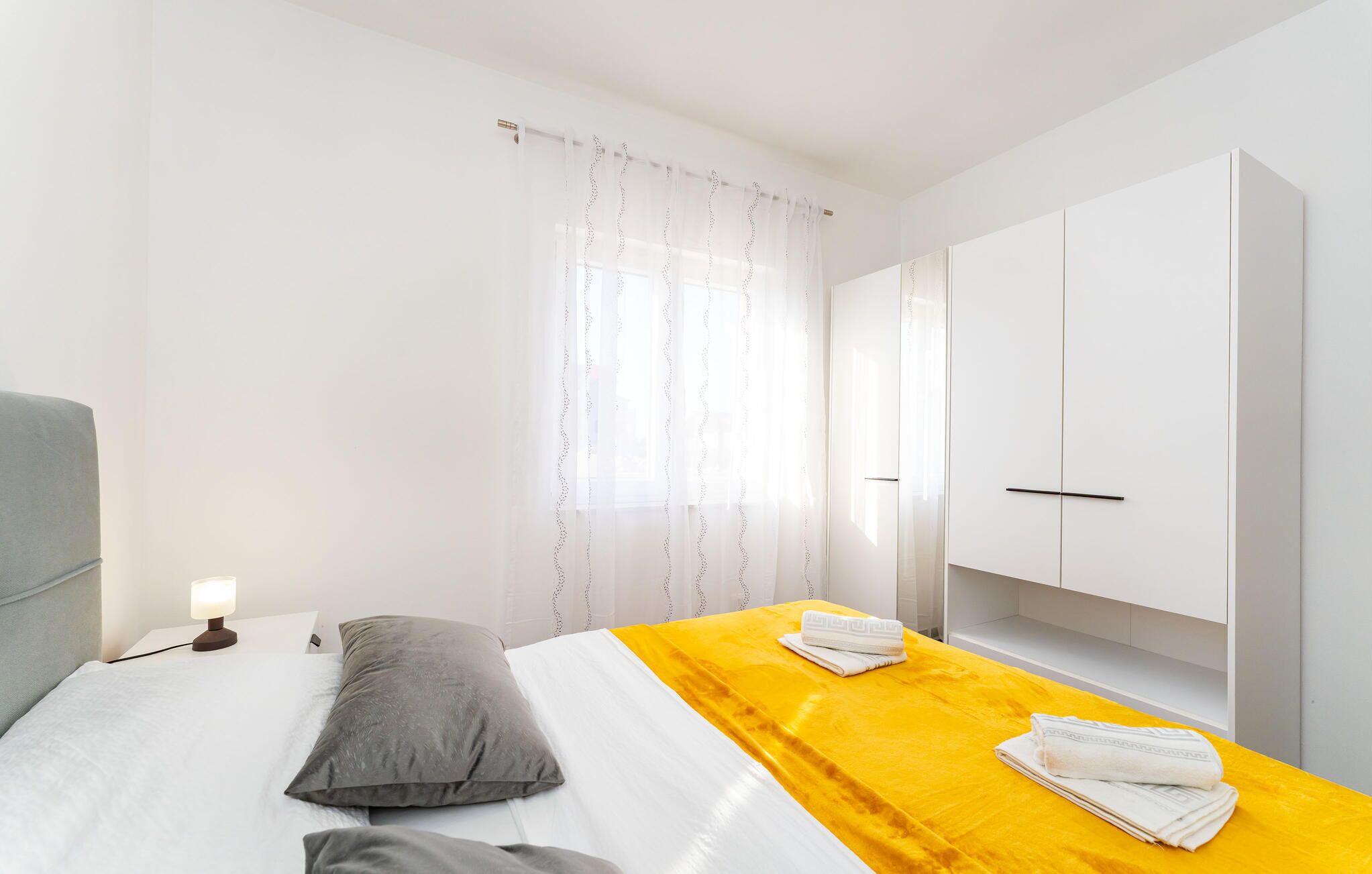 Une chambre d’hôtel avec un lit, une table de chevet, une lampe, une armoire et une fenêtre avec des rideaux.
