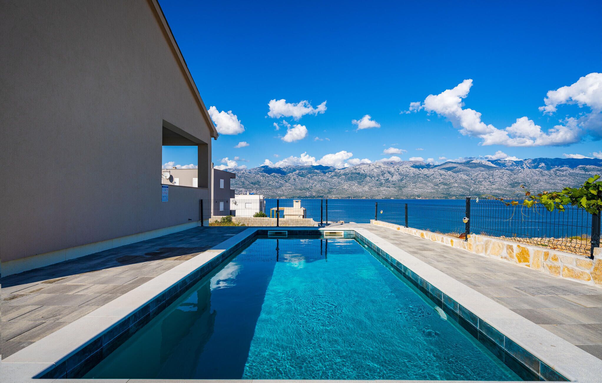 A swimming pool with clear blue water, a view of the sea, and mountains in the background.