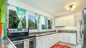 Une cuisine avec des meubles blancs, un fourneau et un tapis à motifs floraux rouges.