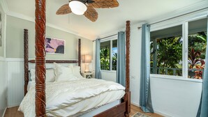 Un lit à baldaquin avec un ventilateur de plafond, une table de chevet avec une lampe et une fenêtre avec des rideaux.