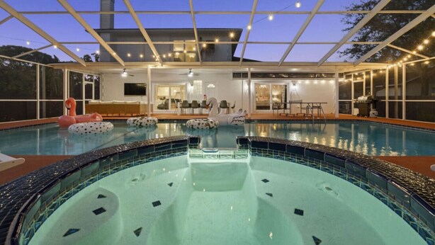An indoor swimming pool with a hot tub, surrounded by a covered deck area with seating and a dining setup.