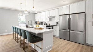 A modern kitchen with white cabinets, stainless steel appliances, and a central island with bar stools.