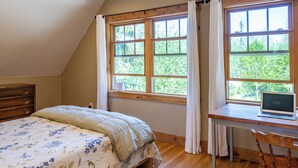 A bedroom with a bed, a desk with a laptop, and large windows with curtains. - Tranquil, private Whidbey Island apt.  Level 2 charging station, pet friendly. (Freeland)