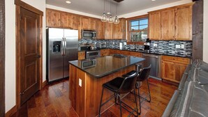Una cocina moderna con armarios de madera, electrodomésticos de acero inoxidable, una isla grande con taburetes de bar y vistas al exterior a través de un ventanal.
