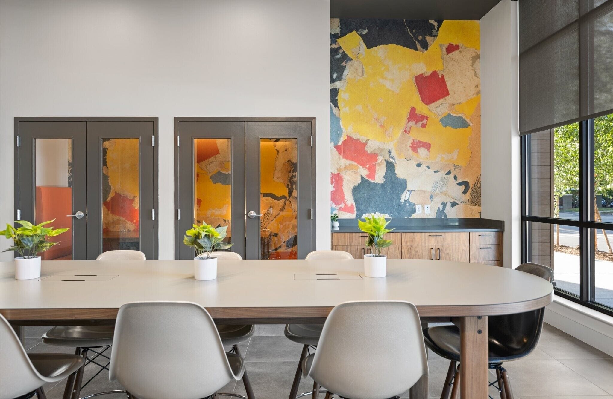 A conference room with a large table, four chairs, and a colorful abstract painting on the wall.