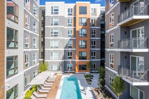 Un moderno edificio de apartamentos con un patio central que cuenta con una piscina, sillas de descanso y plantas en macetas.