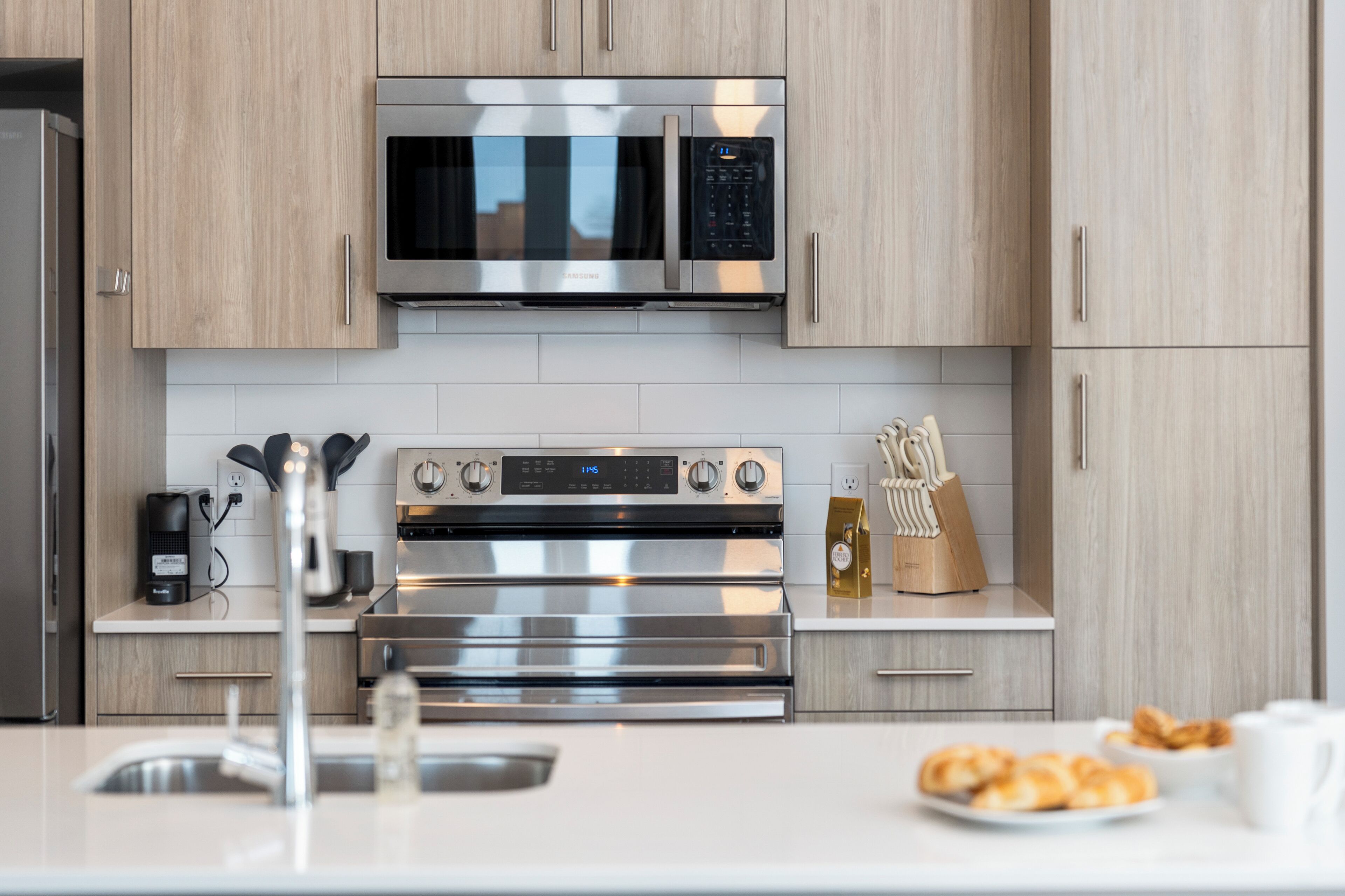 A modern kitchen with stainless steel appliances, wooden cabinets, and a white countertop.