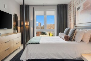 Un dormitorio moderno con una cama grande, un televisor de pantalla plana, un aparador y una ventana con vistas a la ciudad.