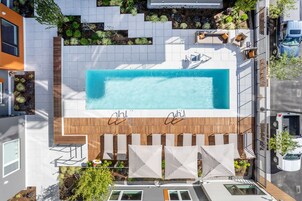 Una piscina en la azotea con terraza de madera, paredes de azulejos blancos y mobiliario exterior.