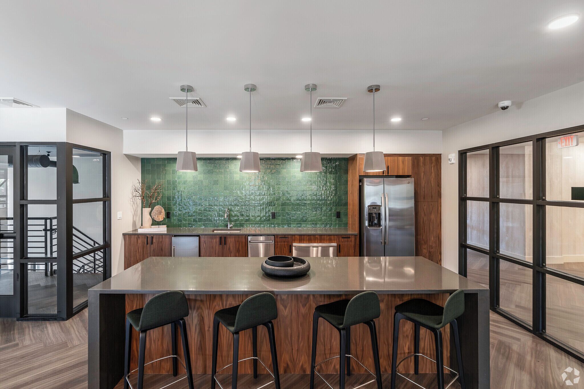 Una cocina moderna con una isla central, luces colgantes y un salpicadero verde.
