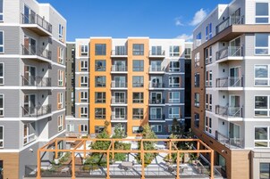 Un edificio residencial de varios pisos con balcones, un patio con asientos y un cielo despejado.