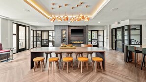 Un vaste espace dédié à la salle à manger, comprenant une grande table en bois, six tabourets en bois et un lustre moderne.