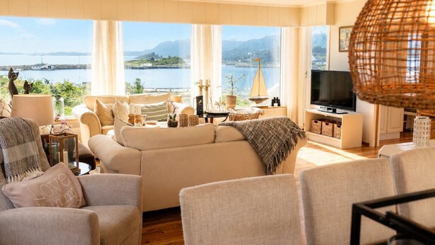 A living room with a sofa, chairs, a TV, and a view of a lake and mountains.