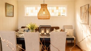 A dining area with a table set for four, a hanging wicker light fixture, and a window with a checkered pattern.