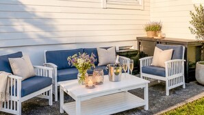 A patio with a white table, blue cushioned chairs, a vase of flowers, a candle, and a champagne bottle.