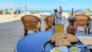 Ett bord med en flaska Blanche de Narmer, ett glas öl, brödskivor och smör på ett bord vid ett café som ligger vid stranden.