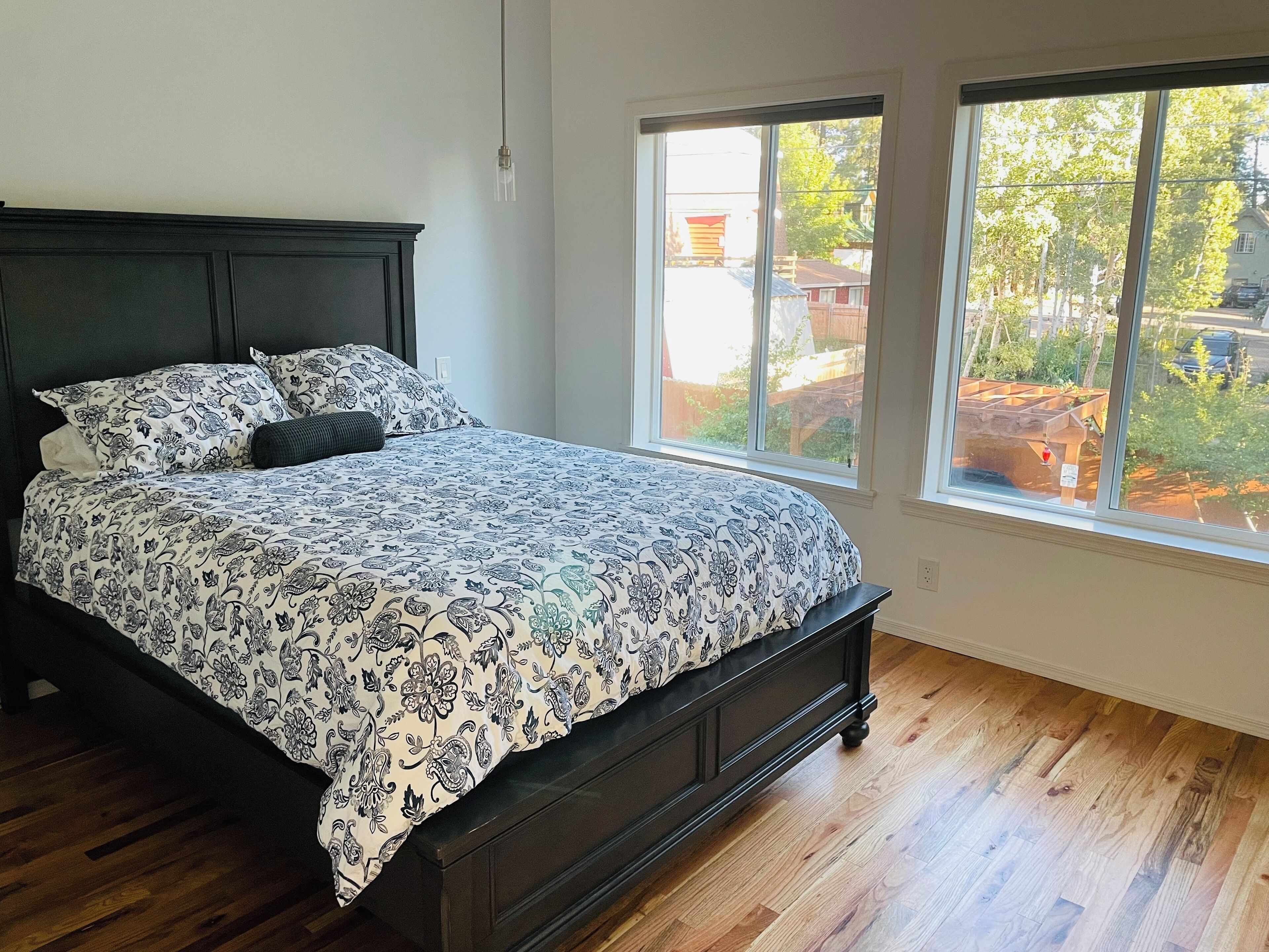 Une chambre à coucher avec un grand lit, une tête de lit en bois foncé et une fenêtre donnant sur un jardin.