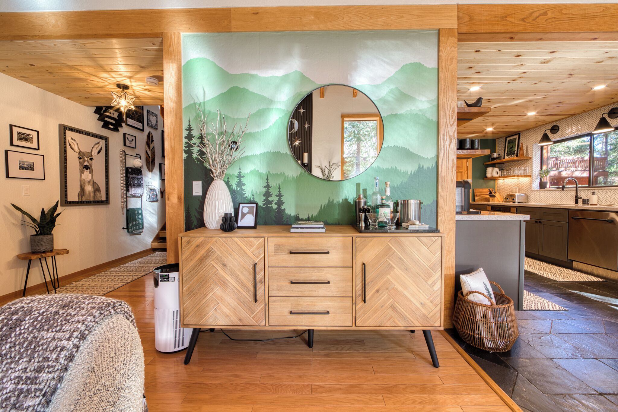 Una sala moderna con un mueble de madera con motivo de espiga, un espejo redondo y un mural decorativo.