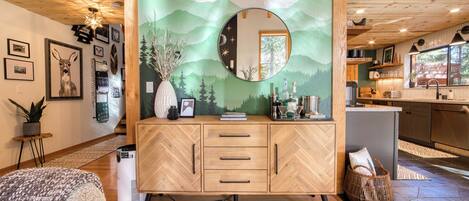 Una sala moderna con un mueble de madera con motivo de espiga, un espejo redondo y un mural decorativo.