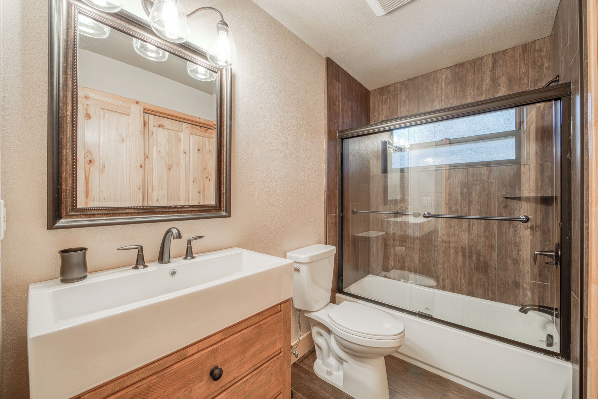 A bathroom with a large mirror, a sink, a toilet, and a glass-enclosed shower.