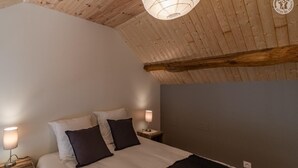 A bedroom with a sloped ceiling, a bed with white and dark pillows, two bedside lamps, and a wooden headboard.
