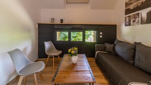 A modern living room with a wooden coffee table, a grey sofa, and a white chair. There is a window with a view of greenery outside.