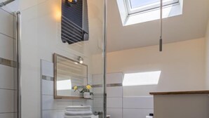 A modern bathroom with a skylight, a wooden vanity, a mirror, and a glass shower enclosure.