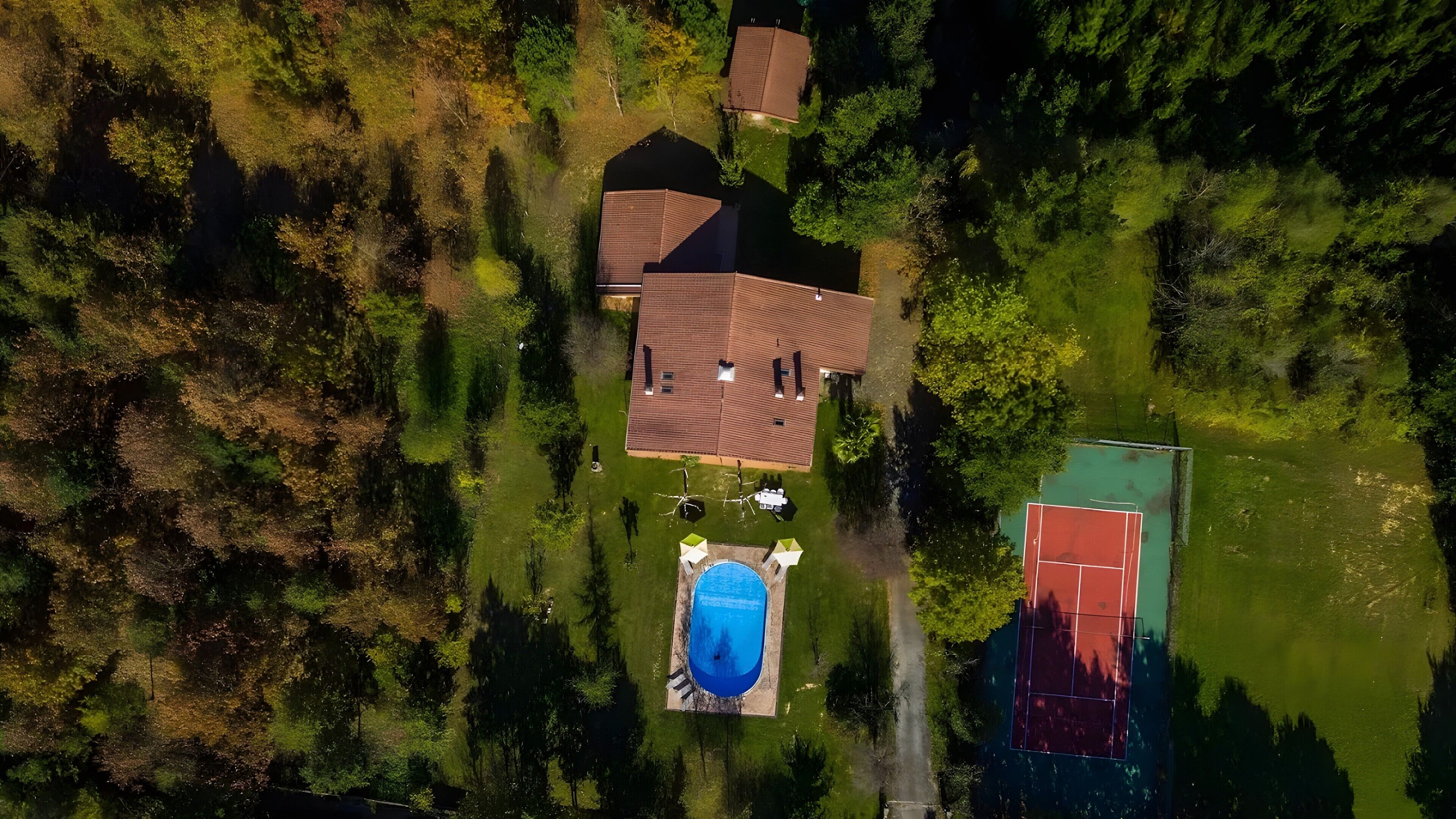 Vista aérea de una zona residencial con piscina, cancha de tenis y varias casas.