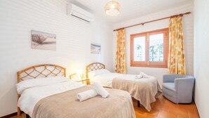 A hotel room with two beds, a chair, a window with curtains, a wall-mounted air conditioner, and a hanging light fixture. - Villa 'Anecs' with Private Garden, Wi-Fi and Air Conditioning (Muro)