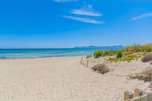 Una playa con agua azul cristalina, orilla arenosa y montañas a lo lejos.