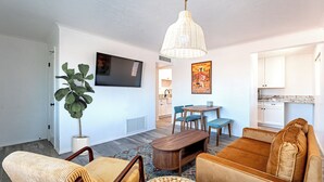 Een woonkamer met een bank, stoelen, een salontafel, een televisie en een eethoek met een tafel en stoelen.