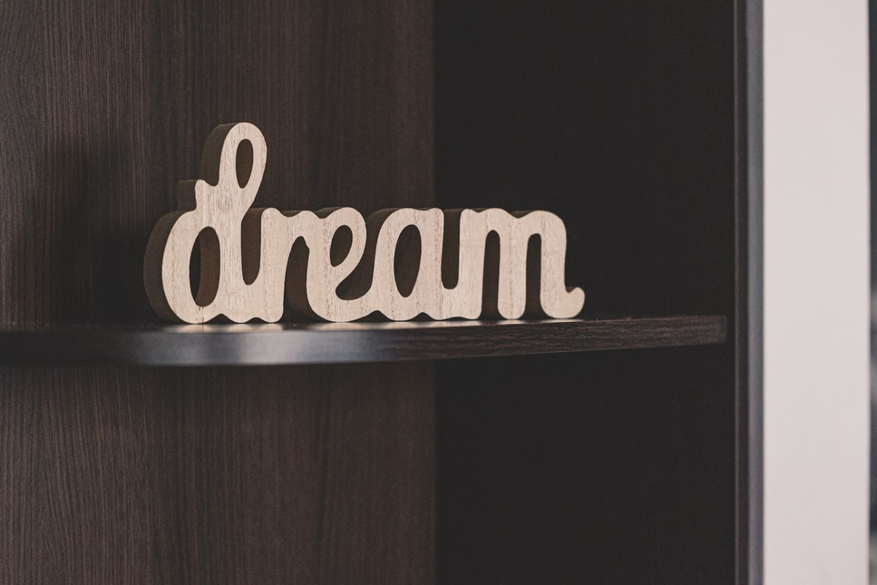 Ein Holzschild mit dem Wort 'dream' auf einer dunklen Holzablage.