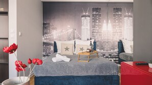 A bedroom with a cityscape mural, a bed with a grey blanket, a bedside table with a tray, and a red side table. - Dream 18 Przytulne Studio Centrum Bydgoszczy (Bydgoszcz)
