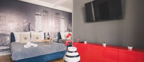 A modern bedroom with a cityscape mural, a large bed, a red dresser, and a flat-screen TV.
