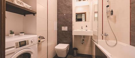 Une petite salle de bain équipée d’un lave-linge, de toilettes, d’un lavabo et d’une baignoire.
