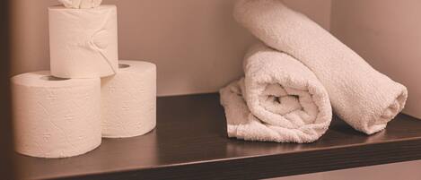 A shelf with three white toilet paper rolls and a rolled white towel.