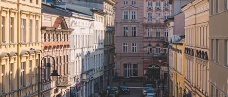 A narrow street lined with historic buildings, featuring a variety of architectural styles and a mix of parked cars.