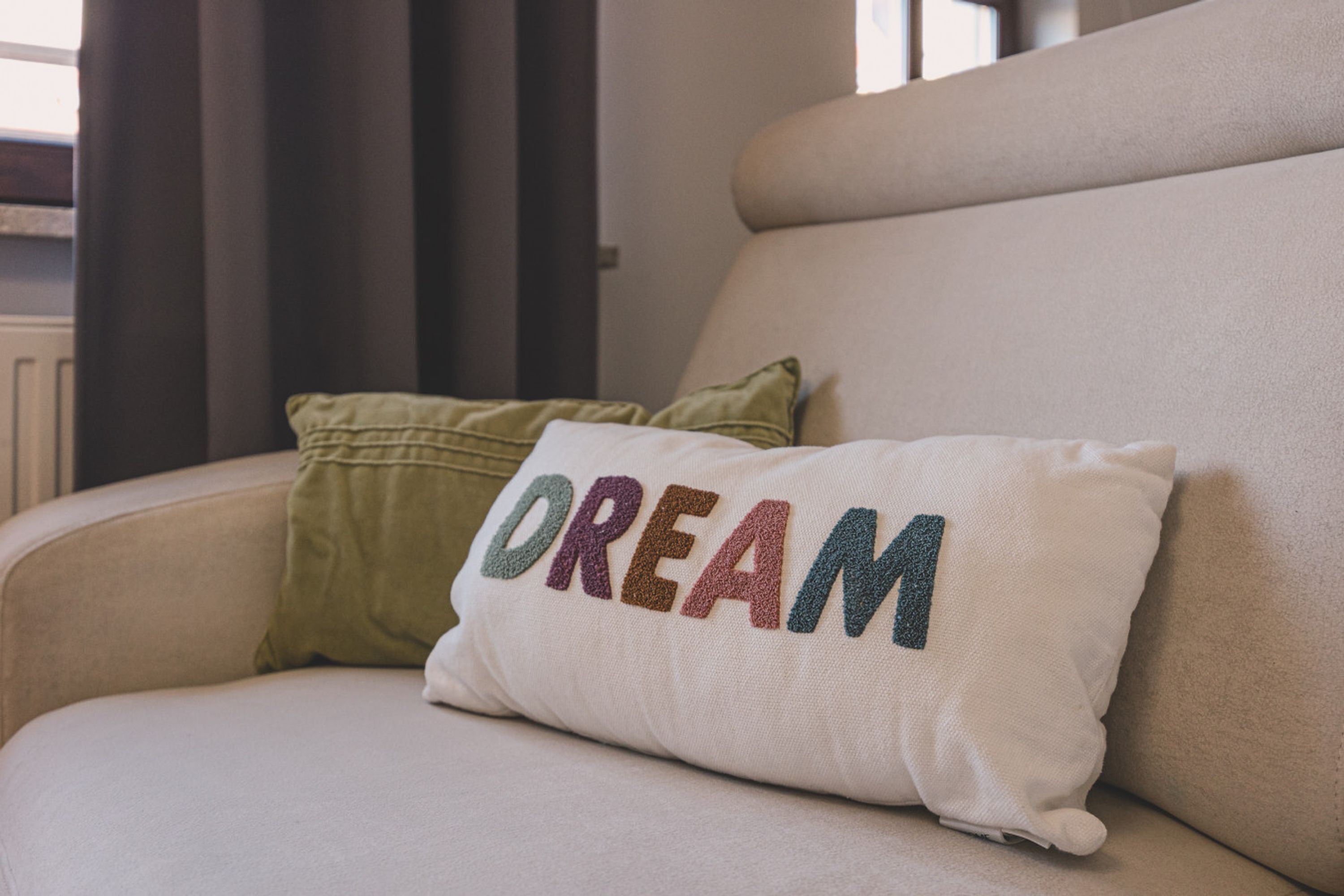 A beige sofa with a white pillow featuring the word "DREAM" in multicolored letters.