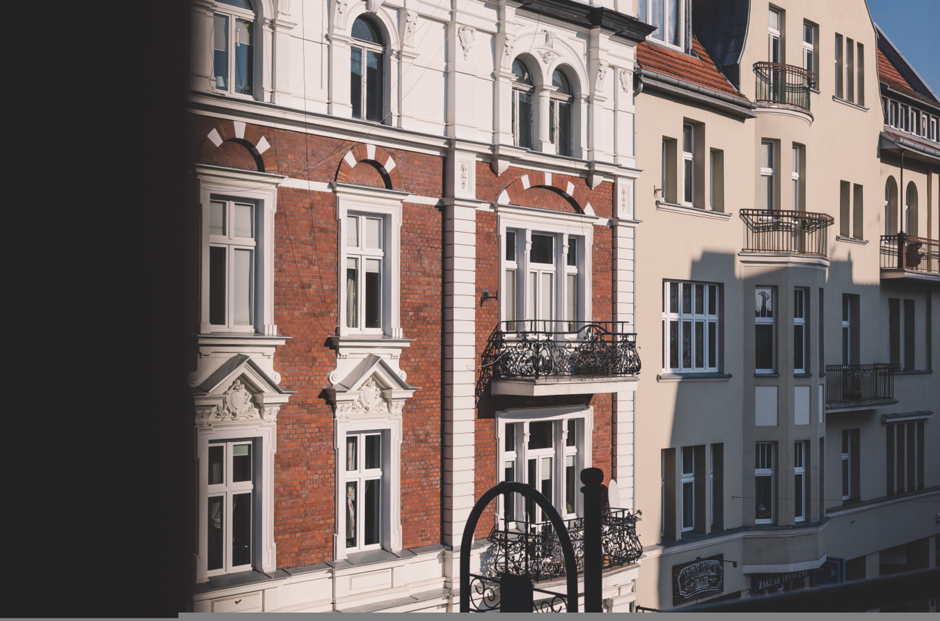 Un immeuble à plusieurs étages dont les façades sont faites d’un mélange de briques et de crépi, avec de grandes fenêtres et des détails architecturaux élaborés.