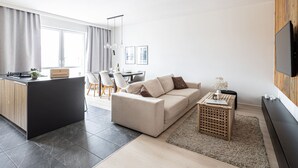 A modern living room with a sofa, a coffee table, and a TV. There is a dining area with chairs and a table. - Humo Idealna Lokalizacja Centrum Gara (Poznan)