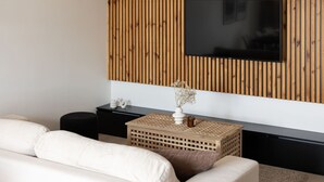 A modern living room with a wooden slat wall, a flat-screen TV, a white sofa, a black side table, and a woven side table. - Humo Idealna Lokalizacja Centrum Gara (Poznan)